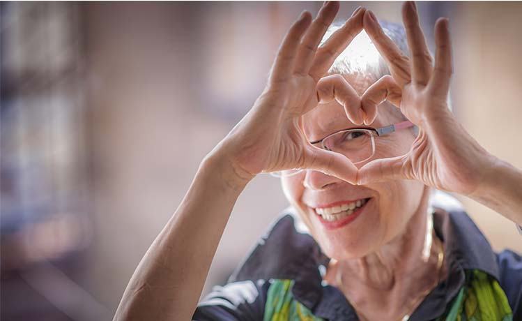 a happy older woman making a heart shape with her hands and peeking through the opening 